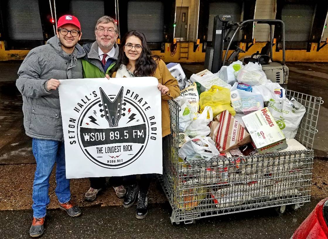 Dalton Allison, Mark Maben and Kali Diamond hold up the WSOU logo in front of their donated food outside of the food bank