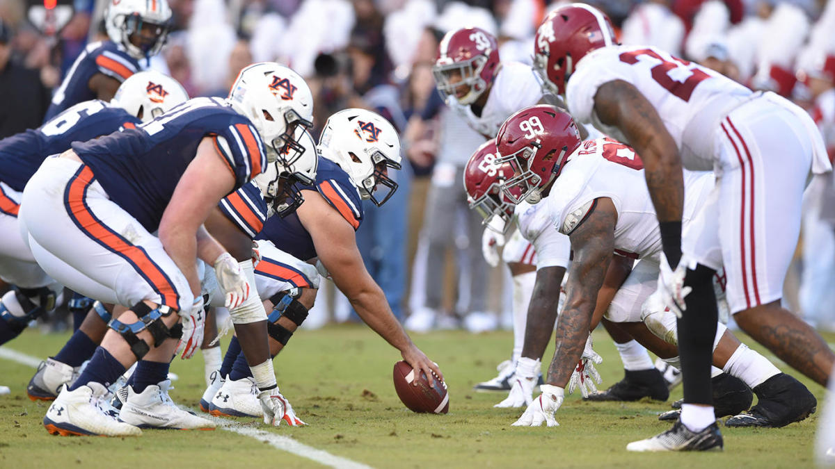 Alabama and Auburn's football teams are at the line of scrimmage during a college football game.