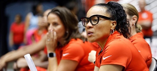 Dawn Staley coaches while sitting on the sideline during a women's basketball game.