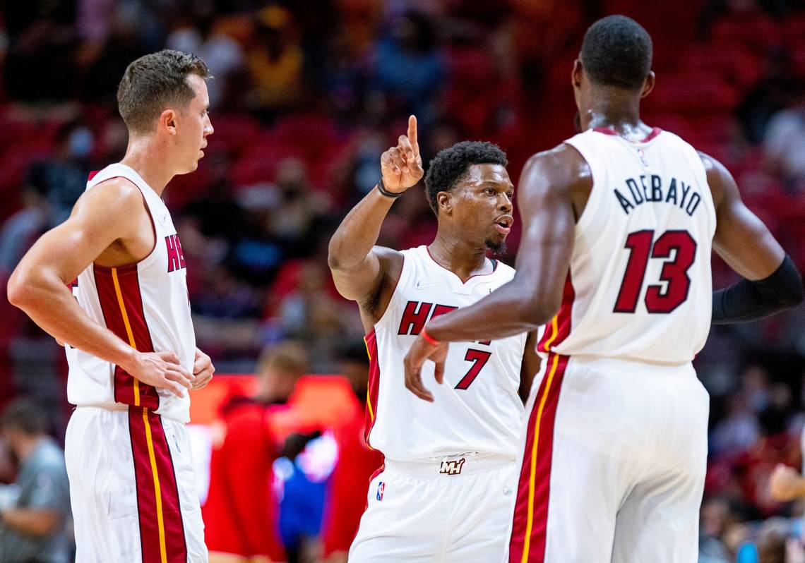 Three players on the Miami Heat stand and talk during an NBA game.
