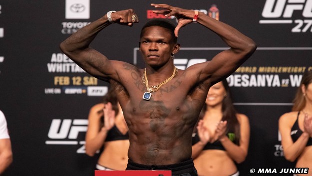 Israel Adesanya flexes during a pre-fight weigh in.