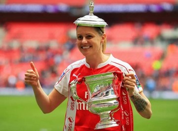 Kelly Smith holds a trophy in celebration with a red jersey worn.