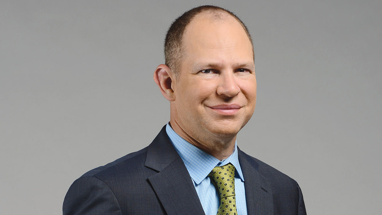 ESPN's Matthew Berry poses for a photo with a clear background behind him.