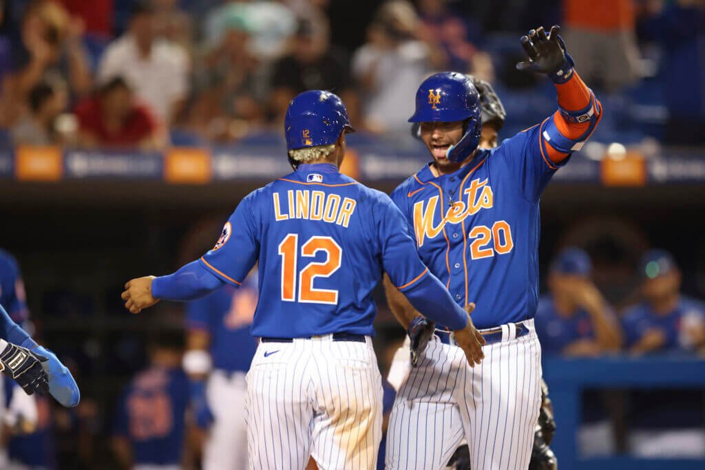 Two New York Mets players celebrate at home plate during a game.