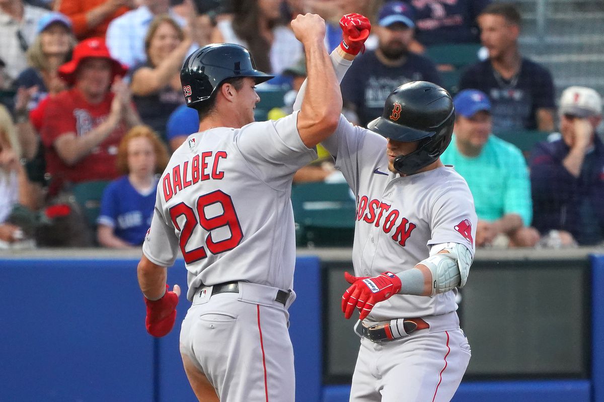 Two Red Sox players celebrate at home plate after scoring a run during a MLB game.