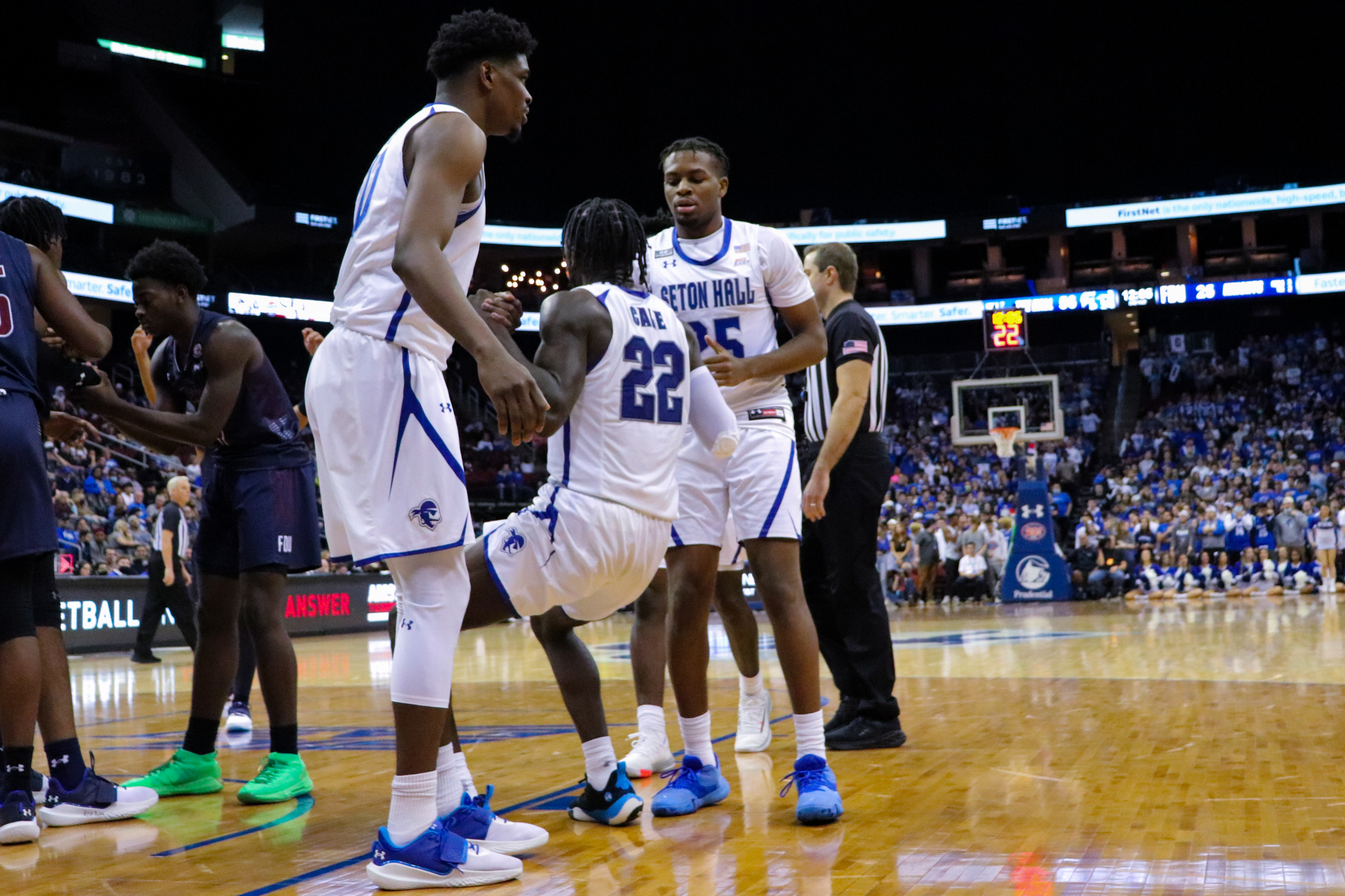 Two Seton Hall men's basketball teammates help another one stand up during a home game.
