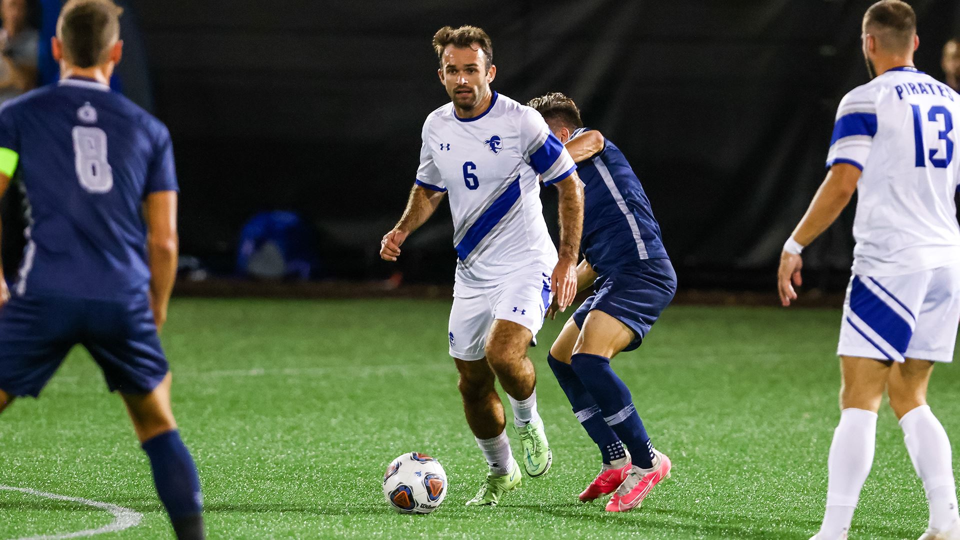 A Seton Hall men's soccer player dribbles the ball against defenders during a game.