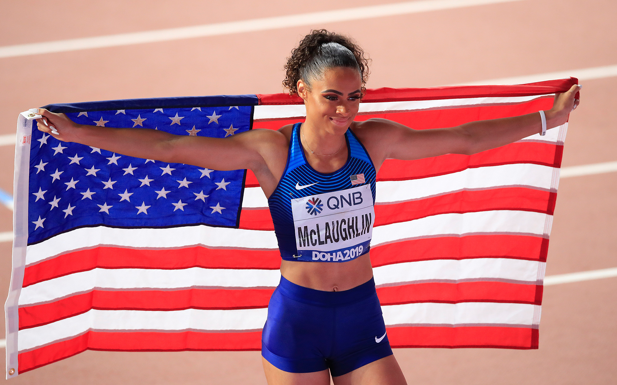Team USA's Sydney McLaughlin holds an American flag over her shoulders as she celebrates a race win.