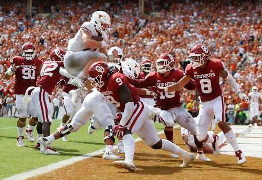 Texas and Oklahoma college football players face off in the endzone.